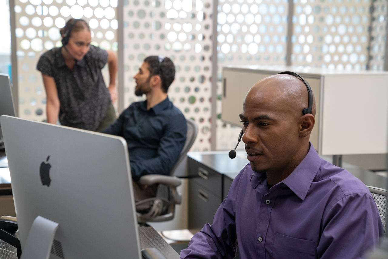 Man in call center with headset looking at computer