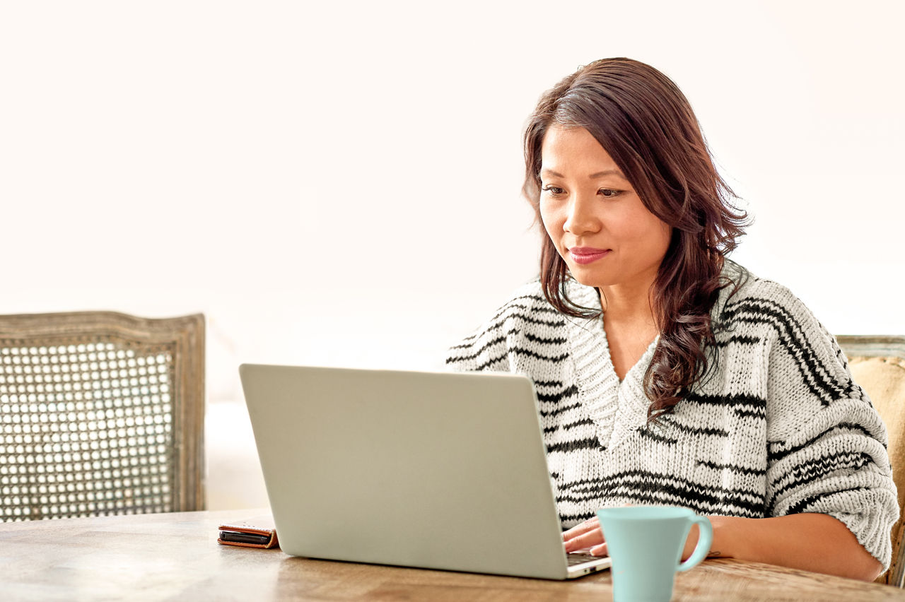 Mid adult woman in her 30s sitting at table and looking at computer, remote working, freelancer, small business