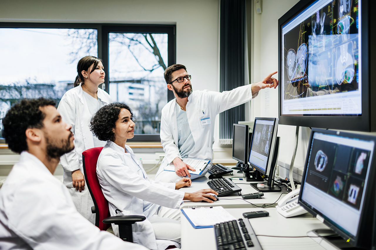 A team of doctors looking at some lab results together on monitors, in an office at the hospital.