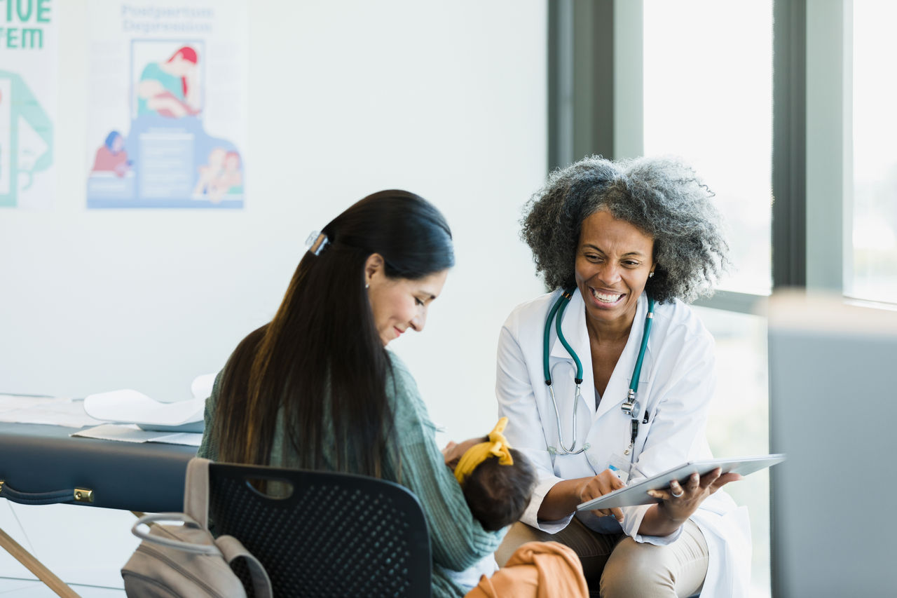 In the middle of a discussion about test results, the mature adult doctor and the new mom smile when the baby girl makes a noise.