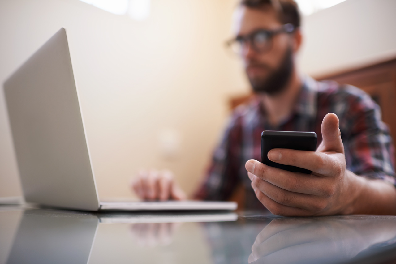 Man at home looking at laptop with phone in hand