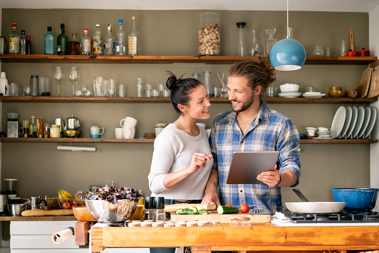 Young couple preparing spaghetti together, using online recipe