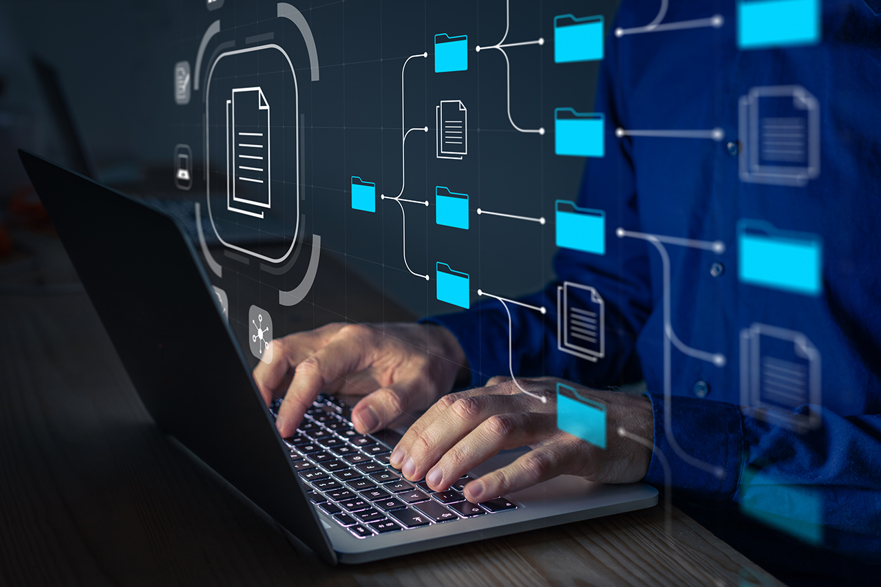 Document Management System (DMS) being setup by IT consultant working on laptop computer in office. Software for archiving, searching and managing corporate files and information. Business processes