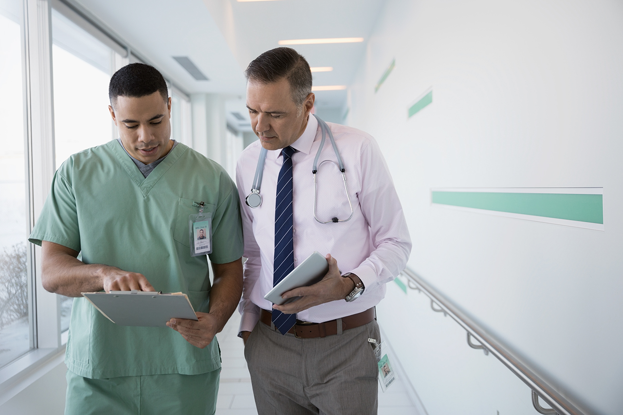 Doctor and nurse with medical record and digital tablet walking and talking in clinic corridor