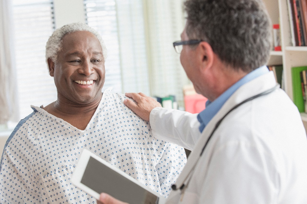 Doctor with digital tablet comforting older man in hospital