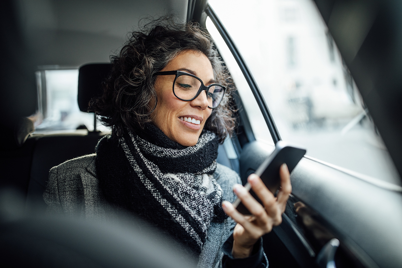 Mature businesswoman reading text message on her cell phone while traveling in a cab. Mid adult female traveling by a taxi and reading text message on her mobile phone.