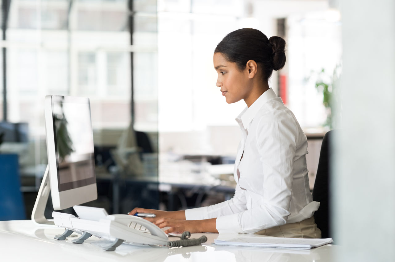 Multi ethnic business woman working with computer at the office. Focused young businesswoman checking email with laptop. Office worker typing on a keyboard in her office.